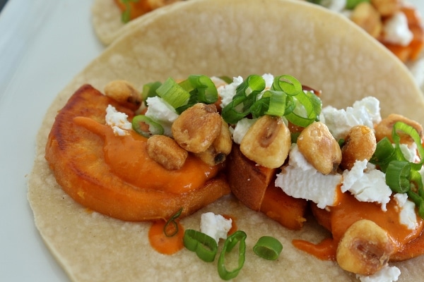 a closeup of a sweet potato taco with corn nuts, scallions, and feta cheese