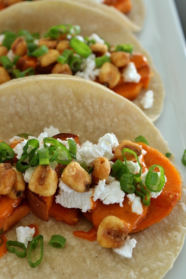 Close up of sweet potato tacos with almond salsa, crumbed feta cheese, corn nuts, and scallions