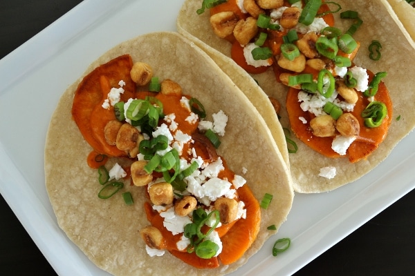 overhead view of sweet potato tacos with almond salsa, crumbed feta cheese, corn nuts, and scallions