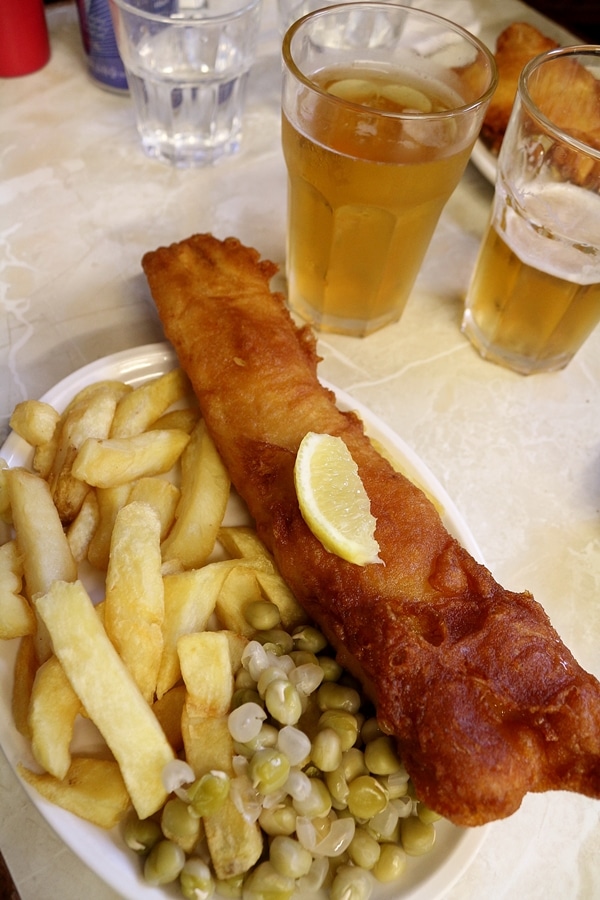 a plate of fish and chips with peas, and glasses of beer