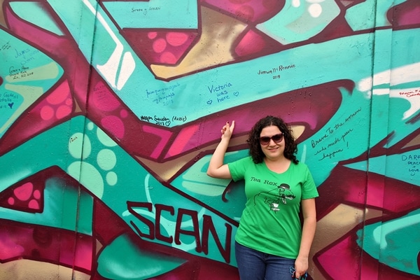 A person posing in front of the Peace Wall in Belfast