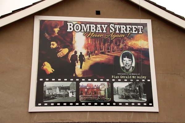 A sign on the side of a building that says Bombay Street Never Again!