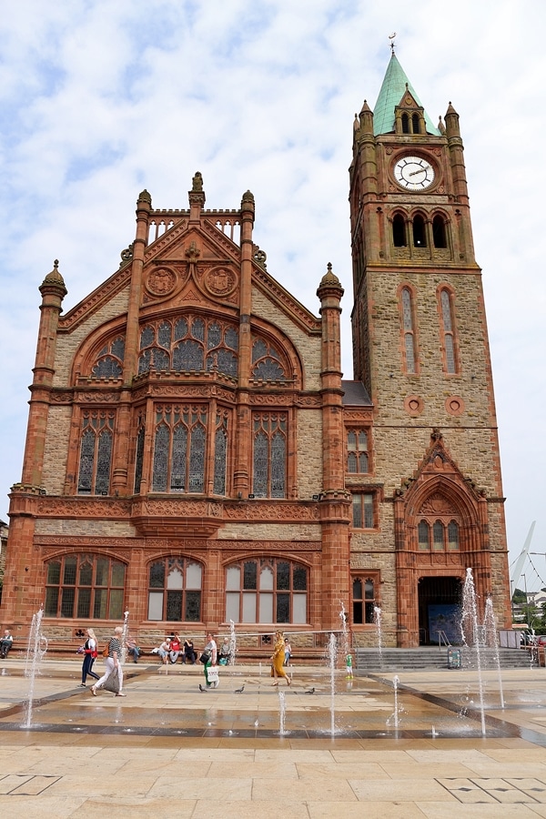 A stone building with a clock tower and a fountain in front