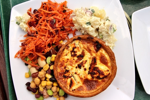 a small quiche on a plate with a variety of salads on the side