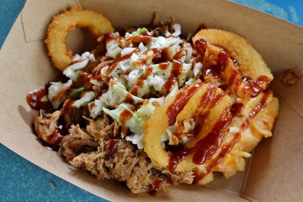 a plate of mac and cheese with pulled pork and onion rings on top