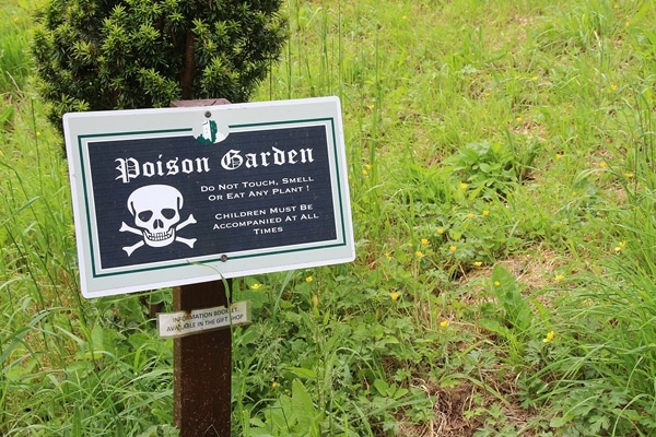 A sign sitting on the grass that says Poison Garden