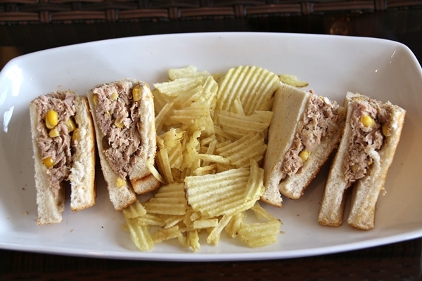 a tuna sandwich cut into quarters on a plate with potato chips