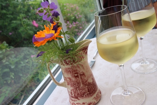 A glass of wine next to a pitcher of flowers