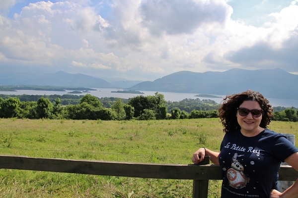 a woman posting in front of a field, lake, and mountains