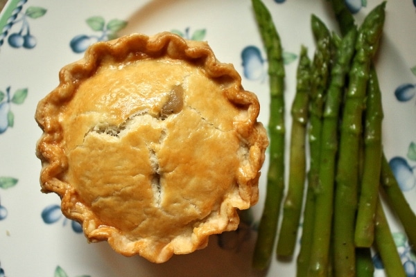 An individual sized savory pie with a golden crust, and asparagus on the side