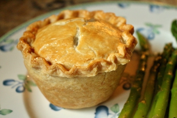 A side view of a small chicken and mushroom pie with a golden crust, and asparagus on the side
