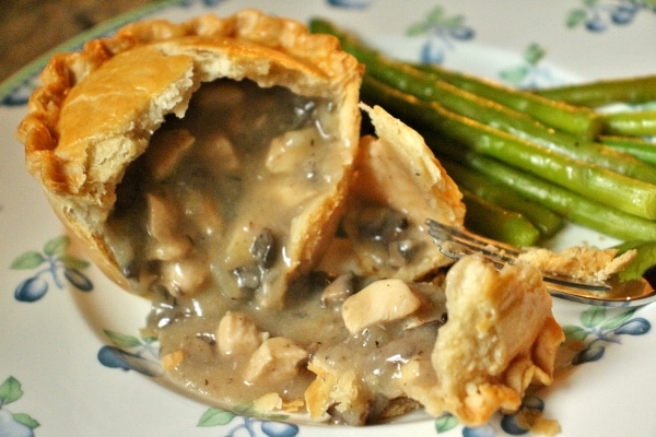 An individual chicken and mushroom pie broken open with the filling spilling out