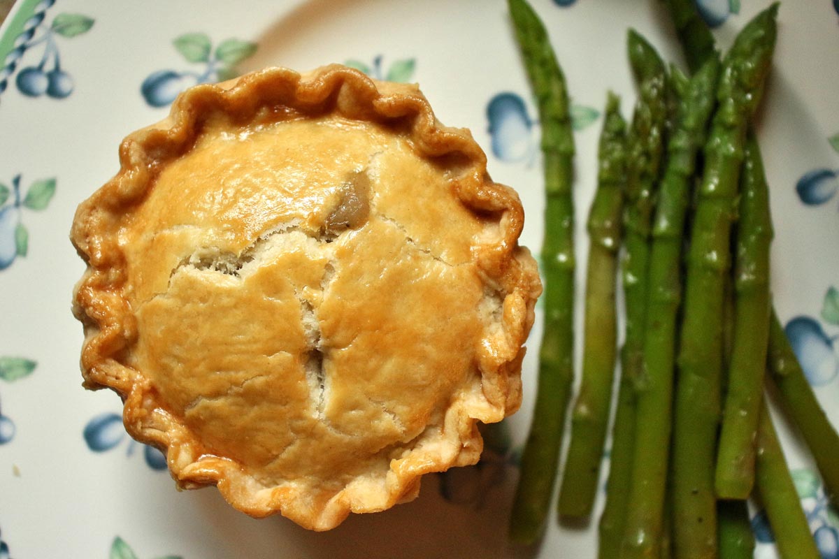 An individual sized savory pie with a golden crust, and asparagus on the side.