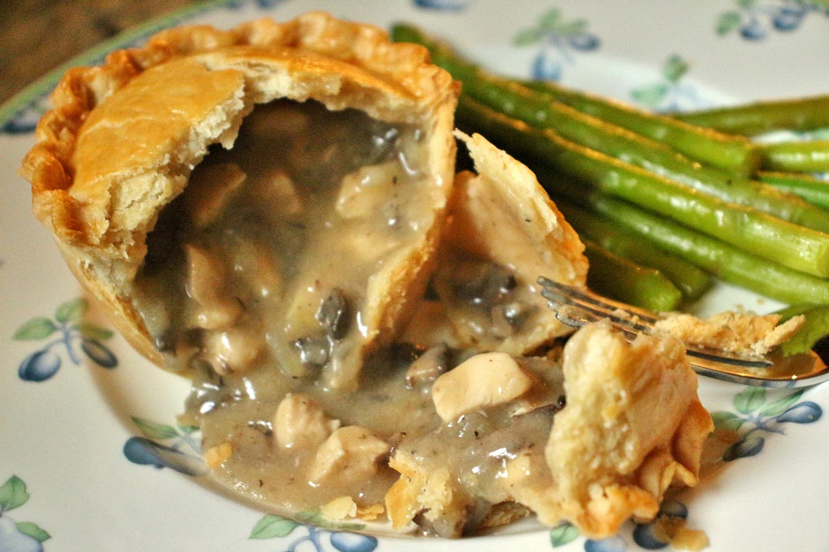 An individual chicken and mushroom pie broken open with the filling spilling out.