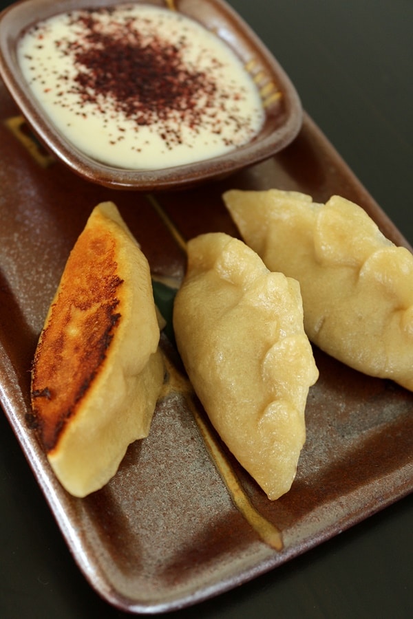 a plate of pan-fried dumplings served with yogurt dipping sauce