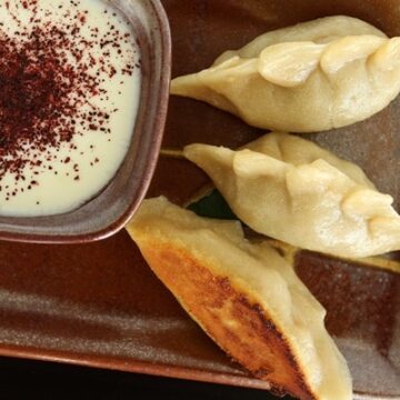 3 manti dumplings on a small burgundy plate with a yogurt dipping sauce on the side