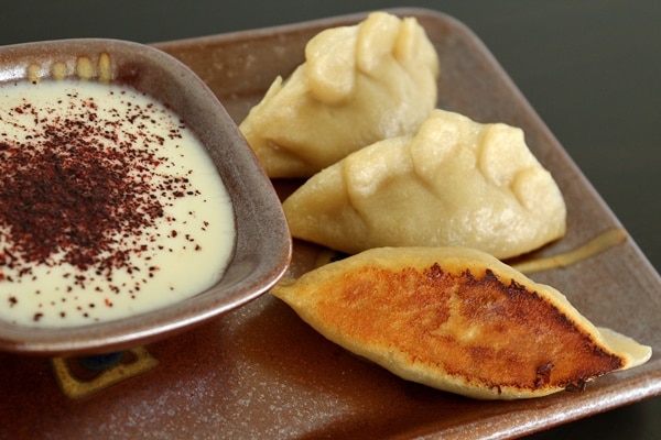 side view of a small plate of manti dumplings with yogurt dipping sauce