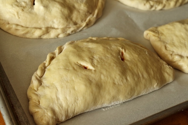 a closeup of unbaked calzones on a baking sheet