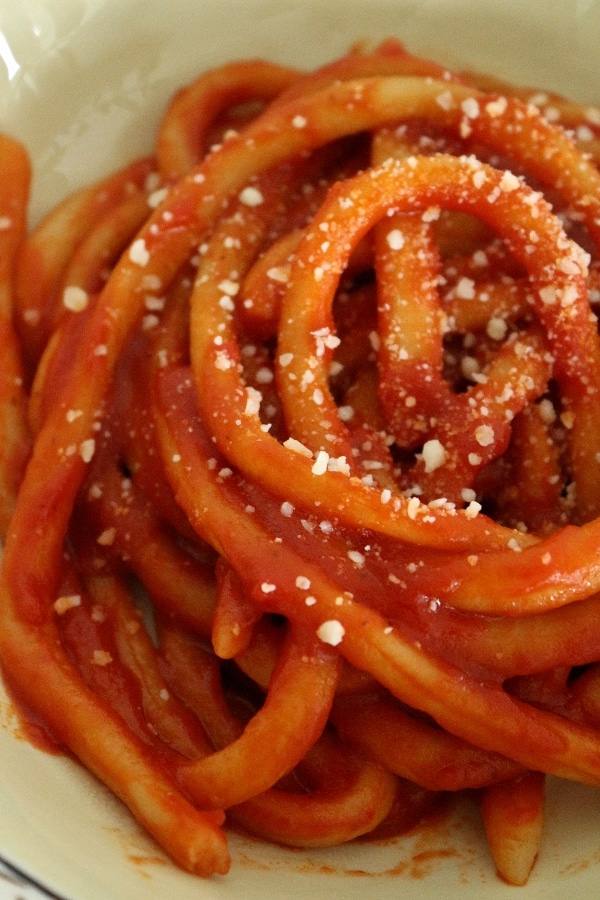 Closeup of hand-rolled pici pasta in tomato sauce, topped with grated cheese