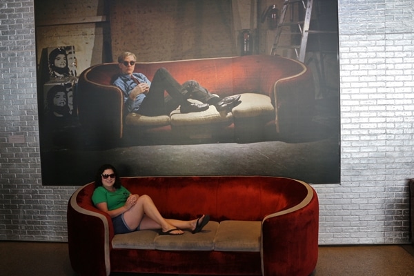 A woman sitting on a couch beneath a painting of a man sitting on a couch