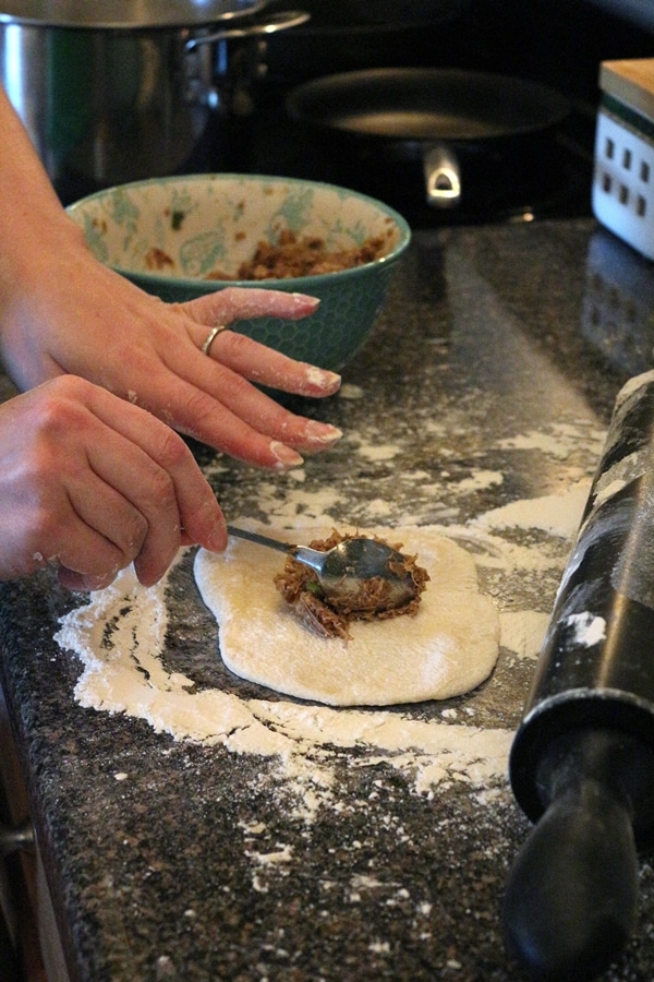 a closeup of hands spooning filling on dough