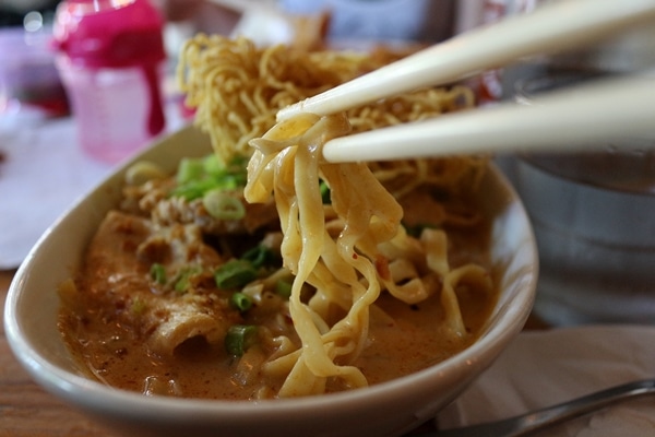 A close up of chopsticks picking up some noodles