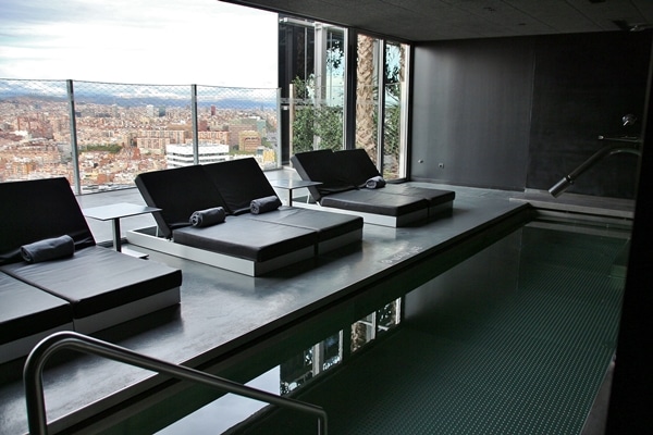 an indoor pool with lounge chairs overlooking Barcelona