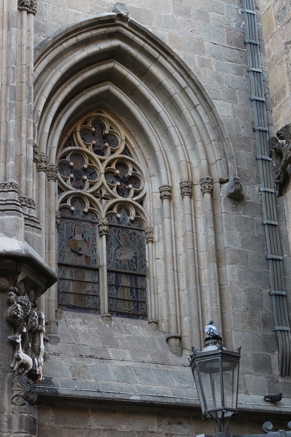 a pigeon on a lamppost in front of an arched window