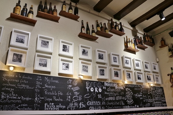 restaurant wall with chalkboard menu, photos, and bottles of wine