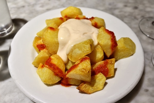 A plate of fried cubed potatoes with red and white sauces on top