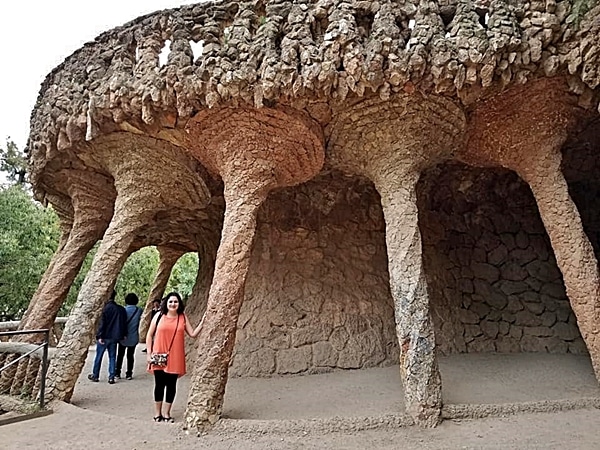 A person standing next to a stone wall with columns in Park Güell