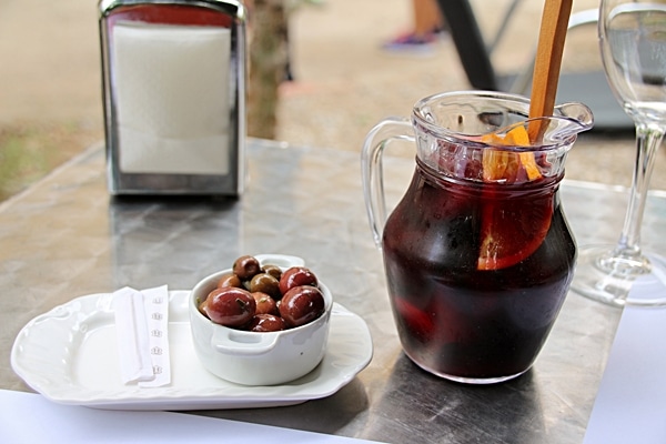 a small glass pitcher of red sangria next to a cup of olives