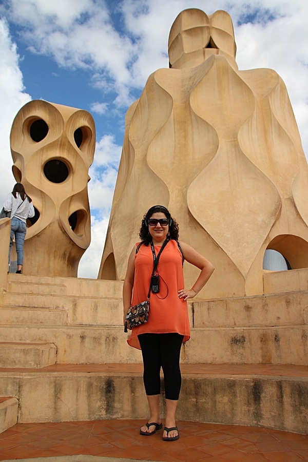 A woman standing in front of a stone chimney on the Casa Milà rooftop