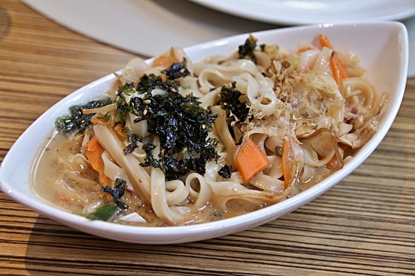 a closeup of rice noodles with broth in an oval dish