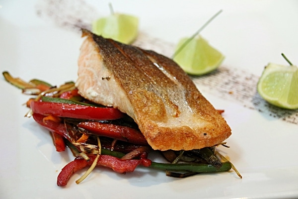 a seared fillet of salmon on top of vegetables on a white plate