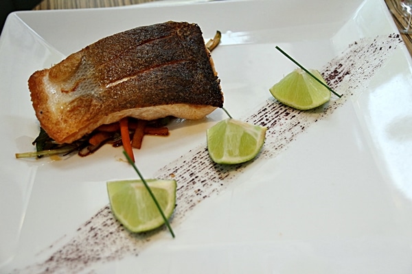 a piece of cooked fish and 3 lime wedges on a white plate