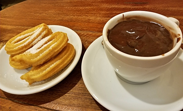 a plate of fried churros next to a cup of hot chocolate for dipping