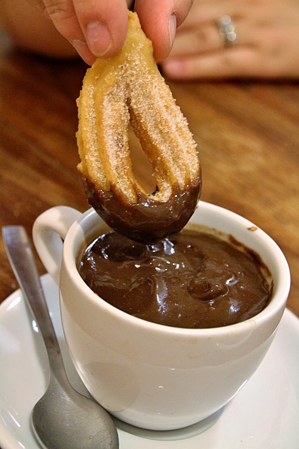 A close up of a churro dipped in melted chocolate