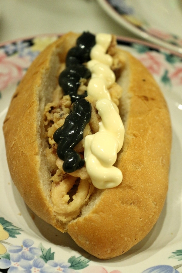 A close up of a fried calamari sandwich with white and black mayonnaise