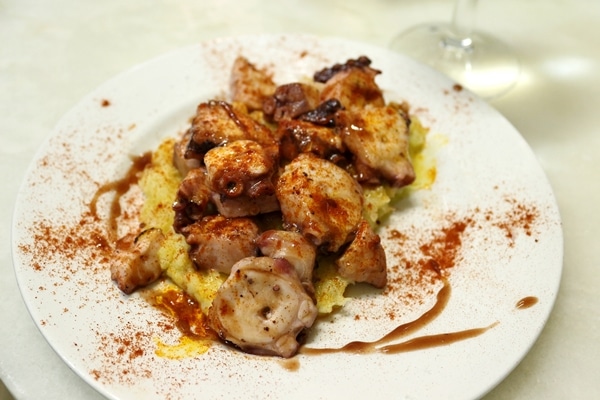 a plate of sliced octopus and mashed potato topped with paprika