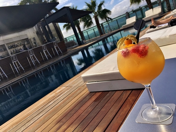 A glass of a fruity cocktail next to a pool with palm trees