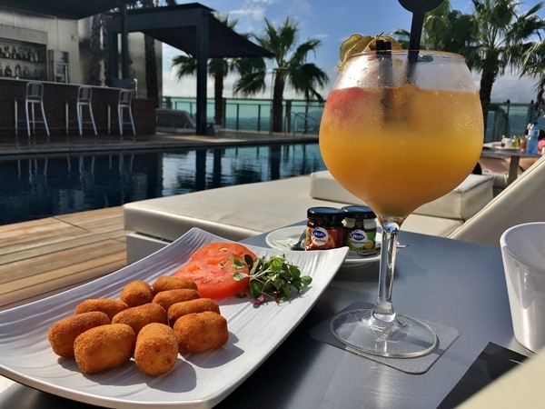 A plate of food and a glass of sangria on a poolside table