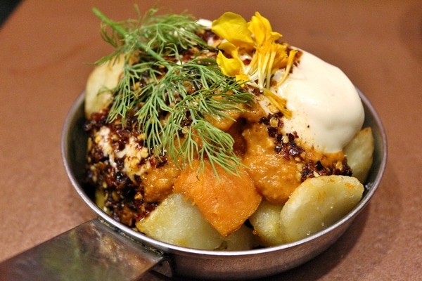 closeup of fried cubed potatoes topped with various sauces and herbs