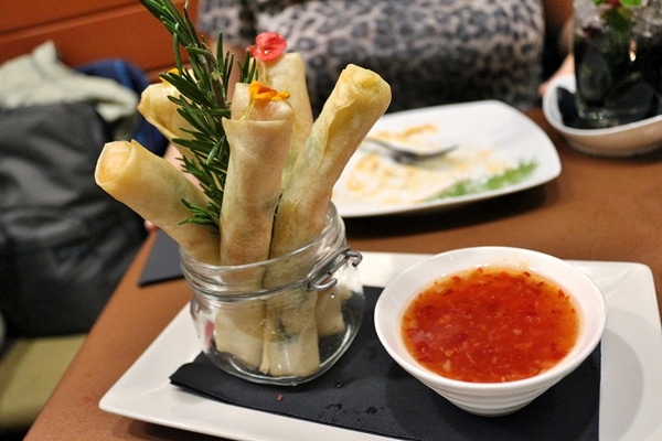 spring rolls sticking up straight in a jar with a bowl of sauce