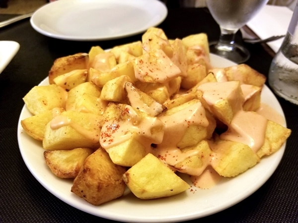 a plate of fried cubed potatoes topped with pink sauce