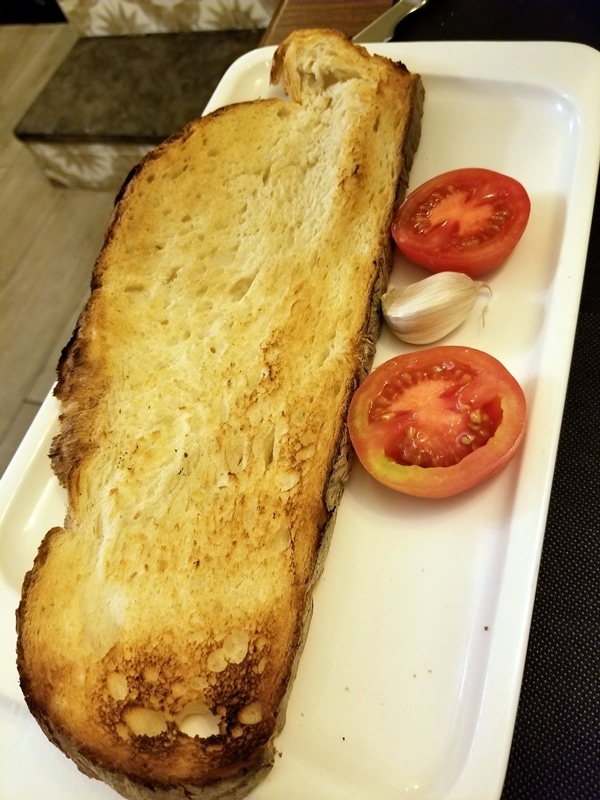 a giant piece of toasted bread with a halved tomato and garlic clove on the side