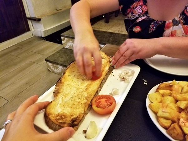 A woman rubbing a halved tomato on a piece of toasted bread