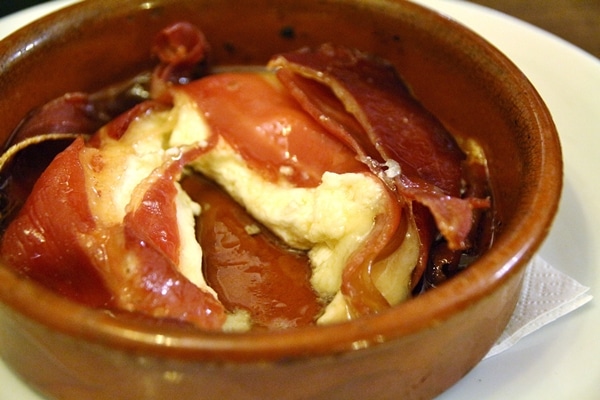 A close up of a dish of hot cheese wrapped in ham