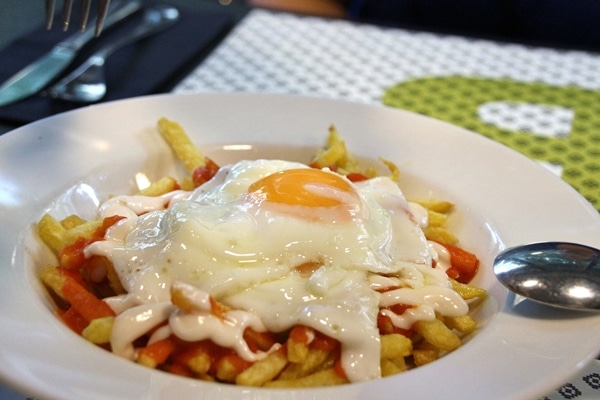 A plate of french fries topped with red and white sauces, and a fried egg