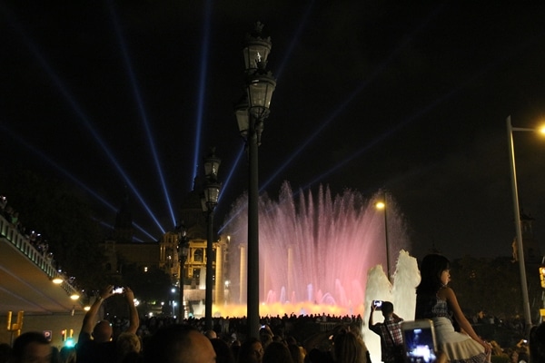 A crowd of people at night in front of a colorful water fountain